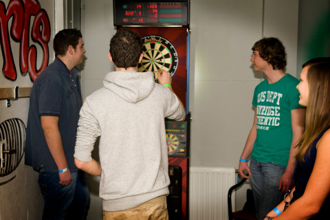 Vier jonge volwassenen spelen samen darts binnenshuis bij de lodge Water Village 4 in Nederland.