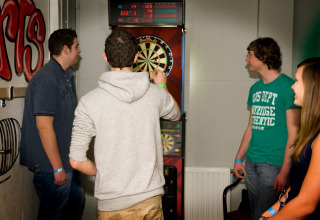 Vier jonge volwassenen spelen samen darts binnenshuis bij de lodge Water Village 4 in Nederland.