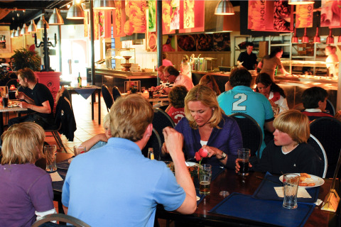 Gezinnen dineren samen in een lodge-restaurant met buffet op de achtergrond en een ontspannen sfeer.