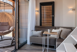 Acogedora sala de casa pequeña en Beach Resort Nieuwvliet-Bad 15 con sofá, silla colgante y ventanales.