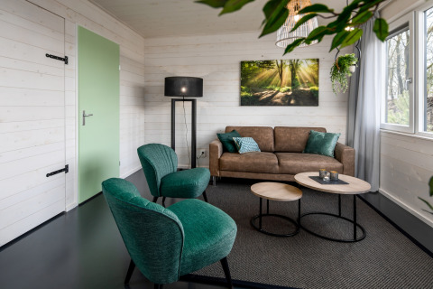 Living room at tiny house Holiday Park Schaijk 3, Netherlands, with green chairs and a brown sofa.