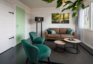 Salon du tiny house Holiday Park Schaijk 3, Pays-Bas, avec fauteuils verts et canapé brun moderne.