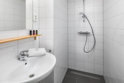 Salle de bain moderne d'une tiny house avec carrelage blanc, douche italienne, lavabo et étagère bois.
