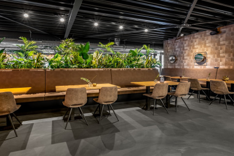Zona pranzo moderna in una tiny house con tavoli in legno, sedie imbottite e molte piante verdi decorative.