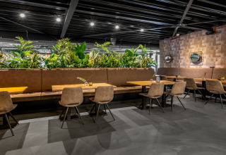 Zona pranzo moderna in una tiny house con tavoli in legno, sedie imbottite e molte piante verdi decorative.