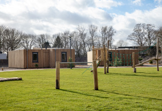 Photo of a tiny house with wooden exterior, green grass, and a wooden playground in the foreground.
