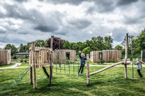 Two children play on a playground in front of tiny houses beneath a dramatic, cloudy sky.