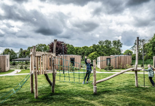 Two children play on a playground in front of tiny houses beneath a dramatic, cloudy sky.