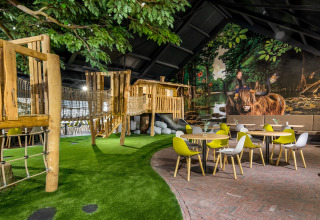 Innenbereich mit Holzspielplatz, Kunstrasen und modernen gelben und weißen Stühlen für Kinder und Familien.