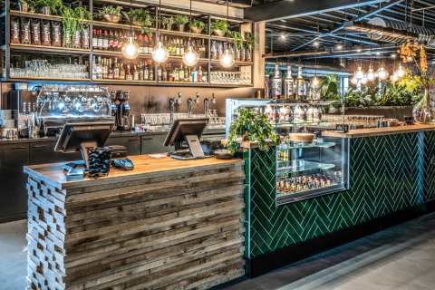Bar moderne dans une tiny house avec plantes, étagères à boissons, éclairage suspendu et comptoir en bois.