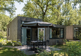 Moderne tiny house Holiday Park «Schaijk 2» i Holland med terrasse og parasol mellem grønne træer.