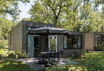 Tiny house moderne Holiday Park «Schaijk 2» aux Pays-Bas avec terrasse, chaises, parasol et arbres verts.