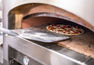 Une pizza est placée dans un four à pierre à l’aide d’une pelle dans une cuisine de tiny house.