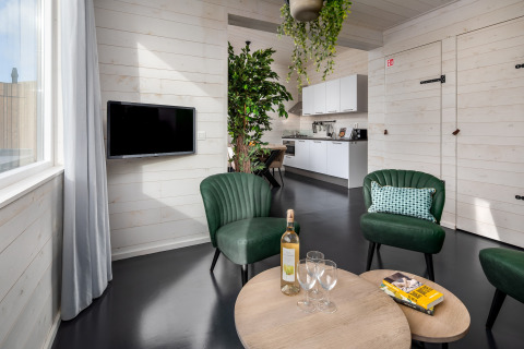 Modern tiny house living room in Schaijk, Netherlands, with green chairs, wine, and open kitchen.