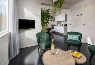Moderne stue i et tiny house med grønne stole, træborde, vinflaske og åbent køkken i Schaijk, Holland.