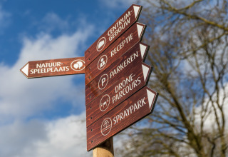Wooden signpost with directions to center, reception, parking, drone course, and spray park in the Netherlands.