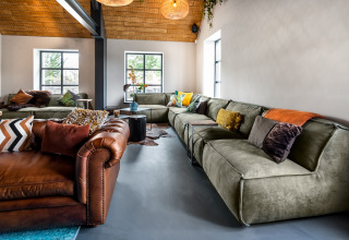 Gemütliches Wohnzimmer im Tiny House im Holiday Park Schaijk 2, Niederlande, mit modernen Sofas und Fenstern.