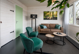 Sala moderna en una tiny house en Holiday Park Schaijk, Países Bajos, con sillones verdes y sofá marrón.