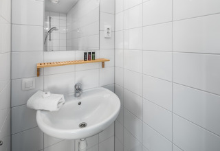 Bagno compatto in Holiday Park Schaijk 1, Paesi Bassi, con lavabo, specchio e mensola in legno.