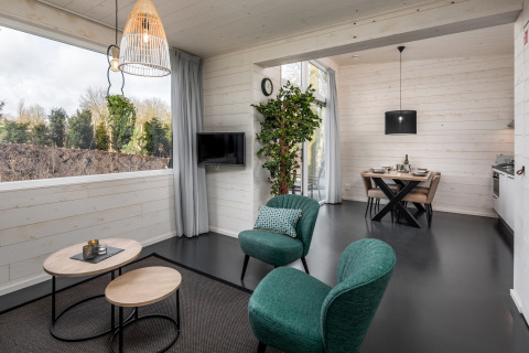 Modern tiny house living room with green chairs, tables, and dining area at Holiday Park Schaijk, Netherlands.