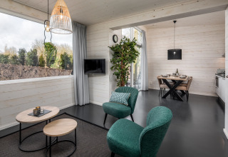 Moderne tiny house-stue med grønne stole, bord, store vinduer og spiseplads i Holiday Park Schaijk.