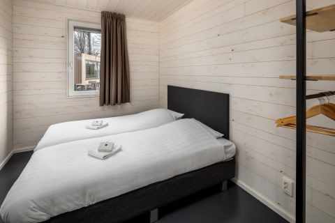 Dormitorio de casa pequeña en Holiday Park «Schaijk 1» en Holanda, con camas individuales y paredes blancas.