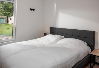 Schlafzimmer in einem Tiny House mit zwei Einzelbetten, großem Fenster und modernem, schlichtem Stil.