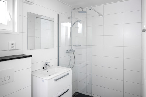 Salle de bain blanche moderne dans une tiny house, avec douche à l'italienne, lavabo et miroir mural.