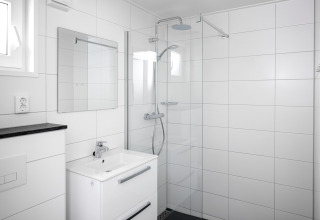 Salle de bain blanche moderne dans une tiny house, avec douche à l'italienne, lavabo et miroir mural.