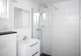 Salle de bain blanche moderne dans une tiny house, avec douche à l'italienne, lavabo et miroir mural.