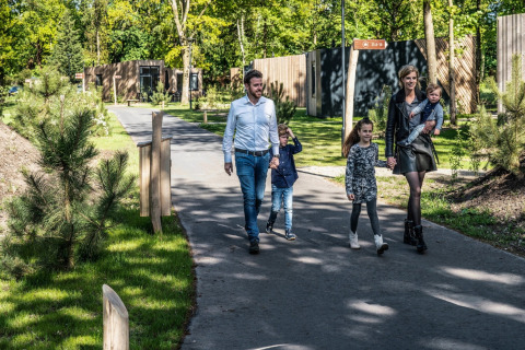 Famille marchant sur un chemin devant des tiny houses, entourés d’arbres et de verdure au soleil.
