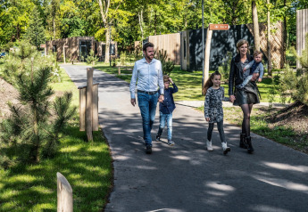 Famille marchant sur un chemin devant des tiny houses, entourés d’arbres et de verdure au soleil.