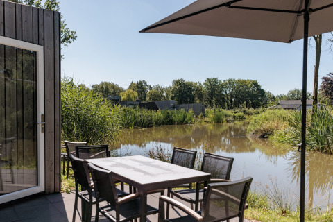Outdoor terrace at Holiday Park Schaijk 4, Netherlands, with table, chairs, umbrella, and water view.