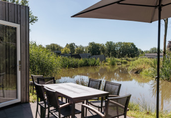 Terrasse extérieure au bord de l'eau, table et chaises sous parasol au Holiday Park Schaijk 4, Pays-Bas.