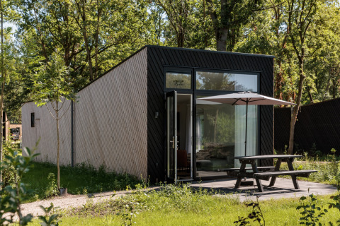 Modern tiny house at Holiday Park Schaijk 7, Netherlands, with terrace, umbrella, and lush surroundings.