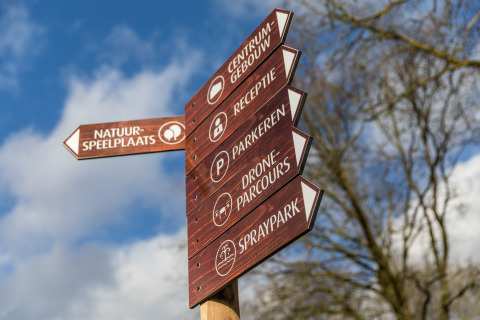 Wooden signpost showing directions to facilities at Holiday Park Schaijk 4, Netherlands, on a sunny day.