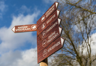 Panneau en bois indiquant les directions des installations au Holiday Park Schaijk 4, Pays-Bas, ciel bleu.