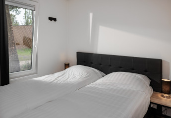 Chambre avec lits jumeaux, têtes de lit noires, tables de chevet et grande fenêtre au Holiday Park Schaijk 5.