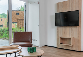 Modernes Wohnzimmer im Tiny House im Holiday Park Schaijk 5, Niederlande, mit TV, Tisch und Fenster.