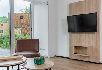 Salon moderne dans une tiny house à Holiday Park Schaijk 5, Pays-Bas, avec TV, fauteuil et grande fenêtre.