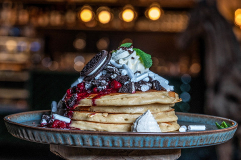 Pila de panqueques con crema batida, Oreos, frutos rojos y dulces en un restaurante acogedor.