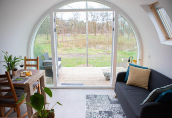 Interior of pod 'De Ree en de Specht' in the Netherlands, showing curved glass door with nature view.