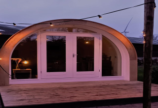 Aftenfoto af pod "De Ree en de Specht" med træterrasse, buet facade og lyssnor, i Holland.