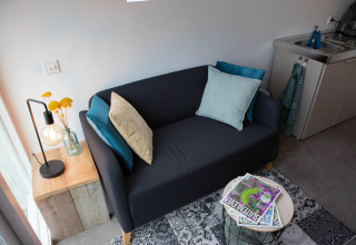 Lille sort sofa med farverige puder i en moderne pod, De Ree en de Specht, Holland, tæt på et tekøkken.