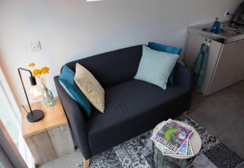 Cozy black sofa with cushions, side table, lamp, and magazines in De Ree en de Specht pod, Netherlands.