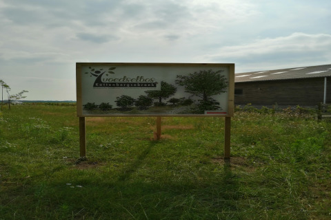 Skilt ved indgangen til fødselsskoven Kattenbergsbroek på en grøn mark nær en lade i Nederlandene.