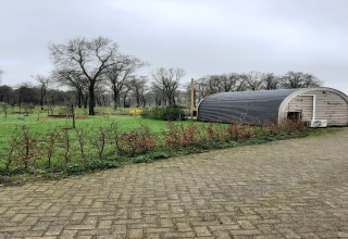 Et pod-hus kaldet 'De Ree en de Specht' på en grøn mark med træer i Nederlandene under en grå himmel.