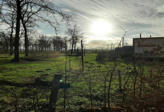 Solrig dag over grønt landskab med træer og et skilt ved podden 'De Ree en de Specht' i Nederlandene.