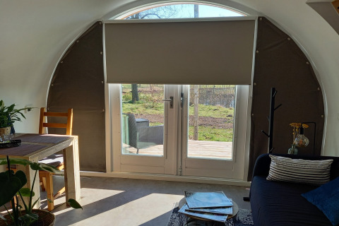Indretning af en hyggelig pod med buet tag, spisestue og udsigt til natur gennem glasdøre i Holland.