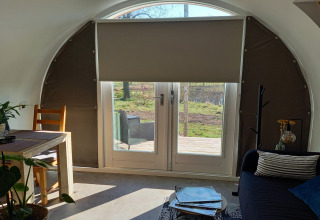 Indretning af en hyggelig pod med buet tag, spisestue og udsigt til natur gennem glasdøre i Holland.